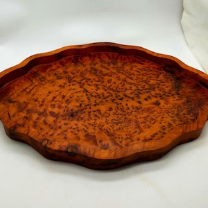 Può includere: Un vassoio in legno fatto a mano con una forma organica unica. Il vassoio è realizzato in legno marrone rossiccio con un caratteristico motivo a radica. I bordi sono delicatamente smerlati, aggiungendo alla sua estetica naturale. Questo vassoio decorativo è ideale per servire o esporre.