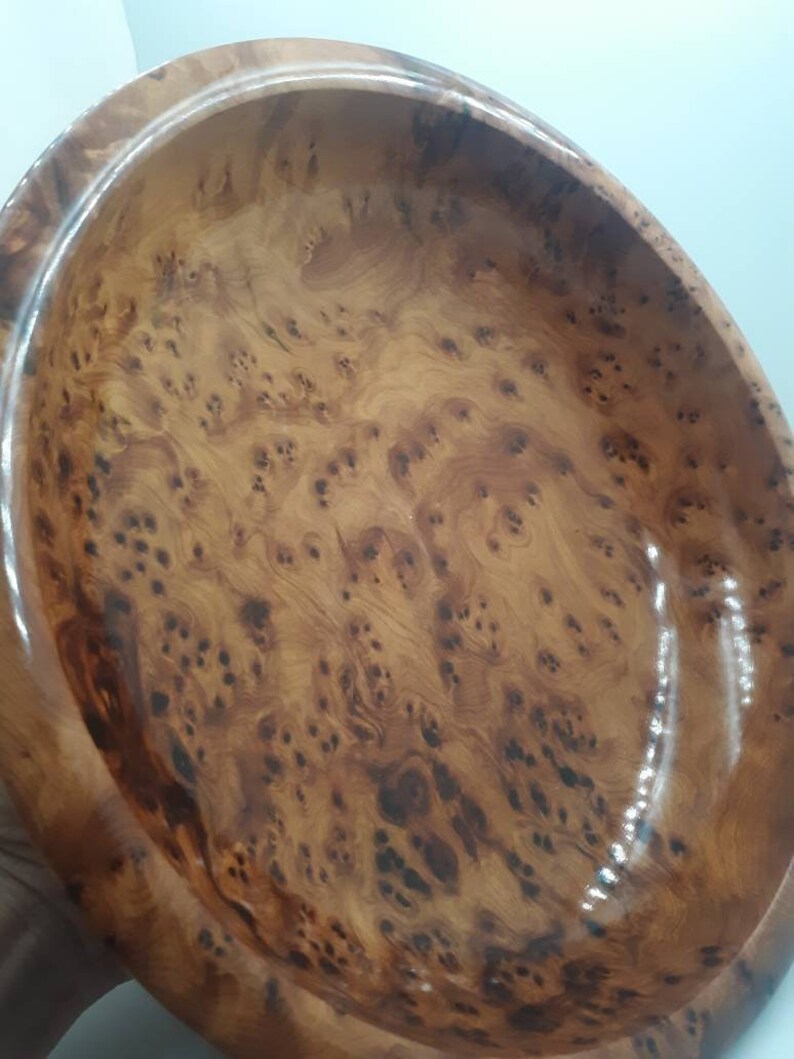 May include: Oval wooden bowl with a glossy finish. The bowl has a natural wood grain pattern in shades of brown and tan. The interior of the bowl is smooth and polished, reflecting light. The bowl is likely used for serving or display.