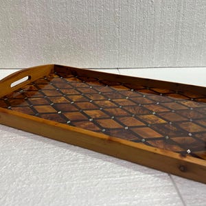 May include: A rectangular wooden serving tray featuring a glossy inlaid surface with a dark brown diamond pattern. The tray has integrated handles on the shorter sides and a smooth, polished finish that highlights the natural wood grain.