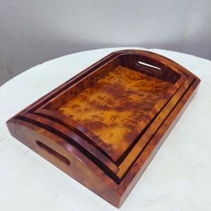 Può includere: Tre vassoi in legno, annidati, con un motivo a venatura del legno naturale. I vassoi hanno bordi arrotondati e una maniglia sul lato.