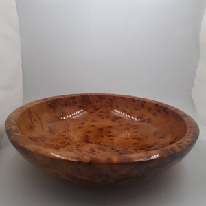 May include: A round wooden bowl with a glossy finish. The bowl is a warm brown colour with a speckled pattern. The bowl has a wide, shallow design.