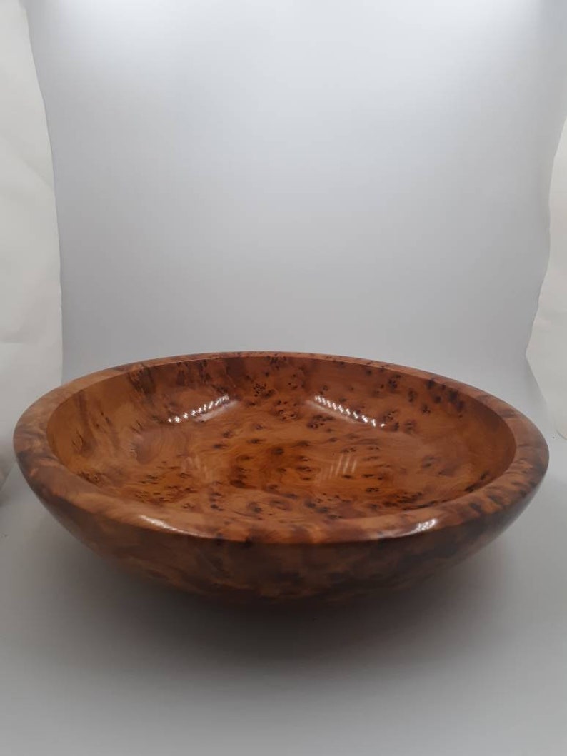 May include: A round wooden bowl with a glossy finish. The bowl is a warm brown colour with a speckled pattern. The bowl has a wide, shallow design.