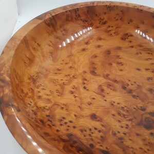 May include: A large, round wooden bowl with a glossy finish. The bowl is made of light brown wood with a unique, swirling grain pattern and dark brown knots. The rim of the bowl is smooth and rounded.