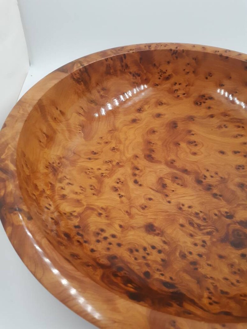 May include: A large, round wooden bowl with a glossy finish. The bowl is made of light brown wood with a unique, swirling grain pattern and dark brown knots. The rim of the bowl is smooth and rounded.