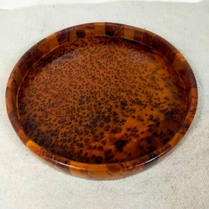 Peut inclure: Un plateau rond en bois aux tons chauds. L'intérieur du plateau présente un motif tacheté unique, tandis que le bord est composé d'une mosaïque de morceaux de bois. Un objet décoratif.
