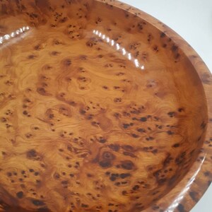 May include: A wooden bowl with a polished finish. The bowl displays a natural wood grain pattern with dark brown knots and swirls against a light brown backdrop. The bowl's rim is rounded and smooth.