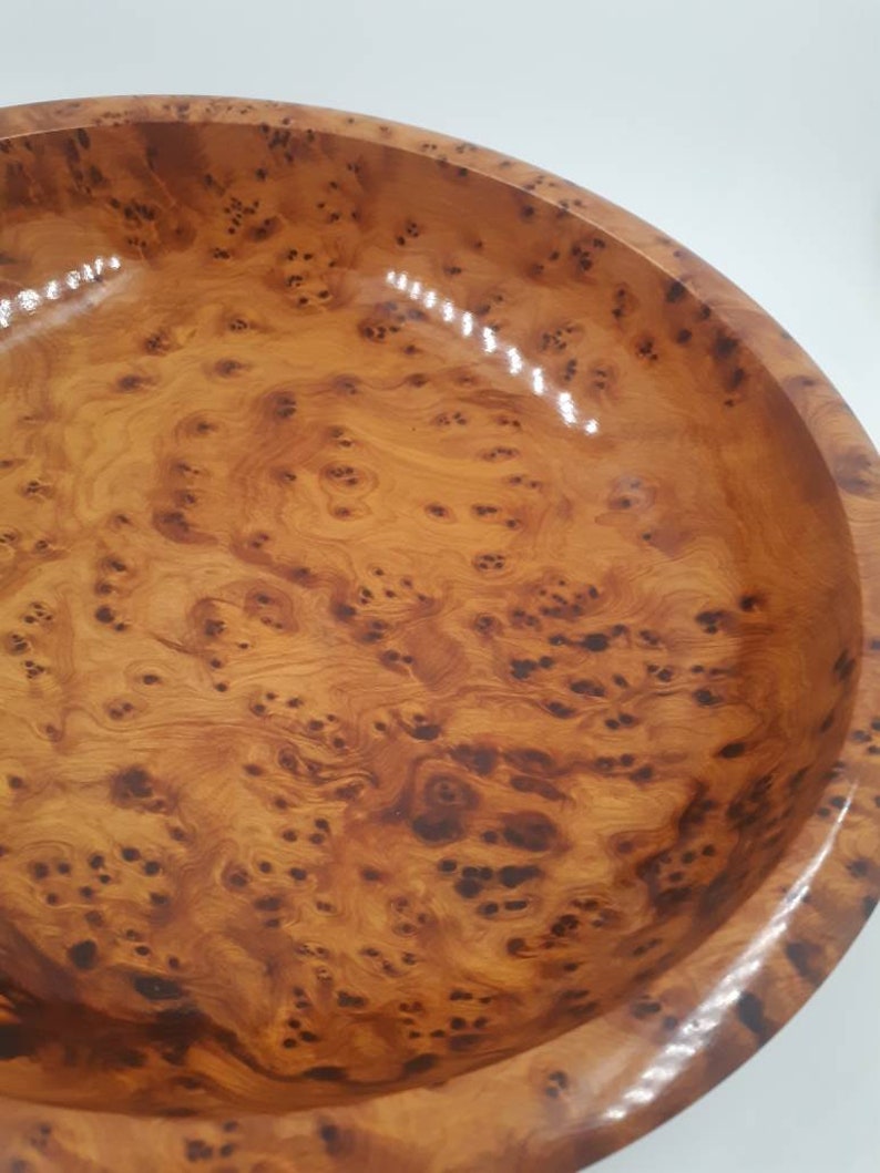 May include: A wooden bowl with a polished finish. The bowl displays a natural wood grain pattern with dark brown knots and swirls against a light brown backdrop. The bowl's rim is rounded and smooth.