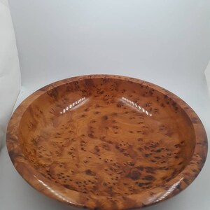 May include: A wooden bowl with a glossy finish, displaying a rich, warm brown colour. The bowl's surface is adorned with a distinctive burl wood grain pattern, featuring intricate knots and swirls. This decorative bowl is suitable for serving or display.