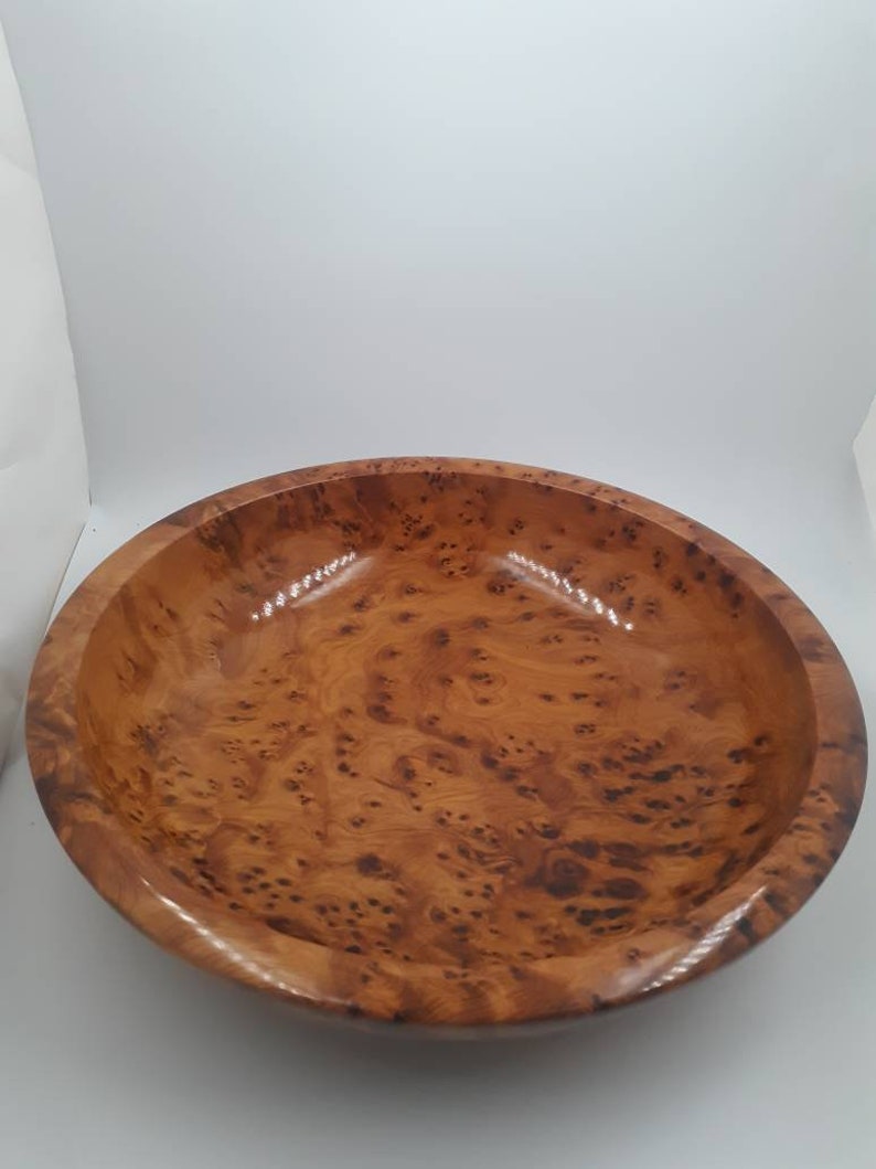 May include: A wooden bowl with a glossy finish, displaying a rich, warm brown colour. The bowl's surface is adorned with a distinctive burl wood grain pattern, featuring intricate knots and swirls. This decorative bowl is suitable for serving or display.