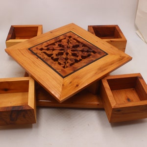 May include: A wooden box with a carved design on the lid and five separate compartments. The box is made of light brown wood with a dark brown inlay around the carved design.