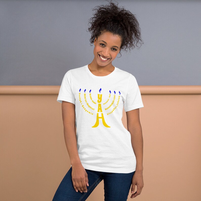 May include: White t-shirt with a gold menorah design. The menorah is made up of the word "YAH" with the Hebrew words for "strength, forgiveness, compassion, kindness, peace, truth, and everlasting love" surrounding it.