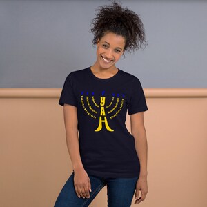 May include: A navy blue t-shirt with a yellow menorah design. The menorah is made up of the word "YAH" with the Hebrew words for the 12 tribes of Israel surrounding it.