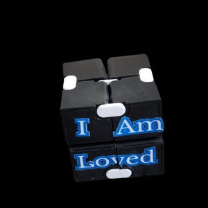 May include: Black fidget cube with white buttons and blue text that reads "I Am Loved".