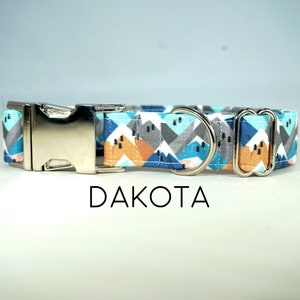 Könnte beinhalten: Ein blaues, graues, orangefarbenes und weißes Hundehalsband mit einer silbernen Schnalle und zwei silbernen D-Ringen. Das Halsband trägt den Schriftzug "DAKOTA".
