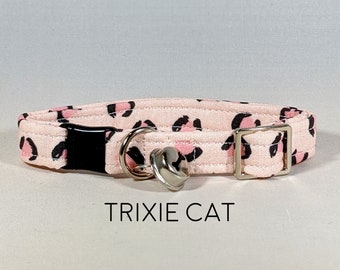 May include: Pink and black leopard print cat collar with a silver bell and a black breakaway buckle. The collar has the text "TRIXIE CAT" printed on it.