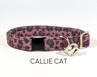 May include: A pink and black leopard print cat collar with a black breakaway buckle and a silver bell.