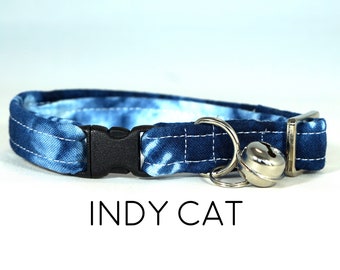 May include: Blue and white tie-dye cat collar with a black buckle and a silver bell. The collar has the text "INDY CAT" printed below it.