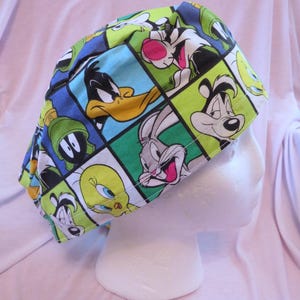 May include: A colorful surgical scrub cap featuring a repeating pattern of cartoon characters, including Bugs Bunny, Daffy Duck, and Sylvester the Cat. The cap is made of a lightweight fabric and is designed to cover the hair during medical procedures.