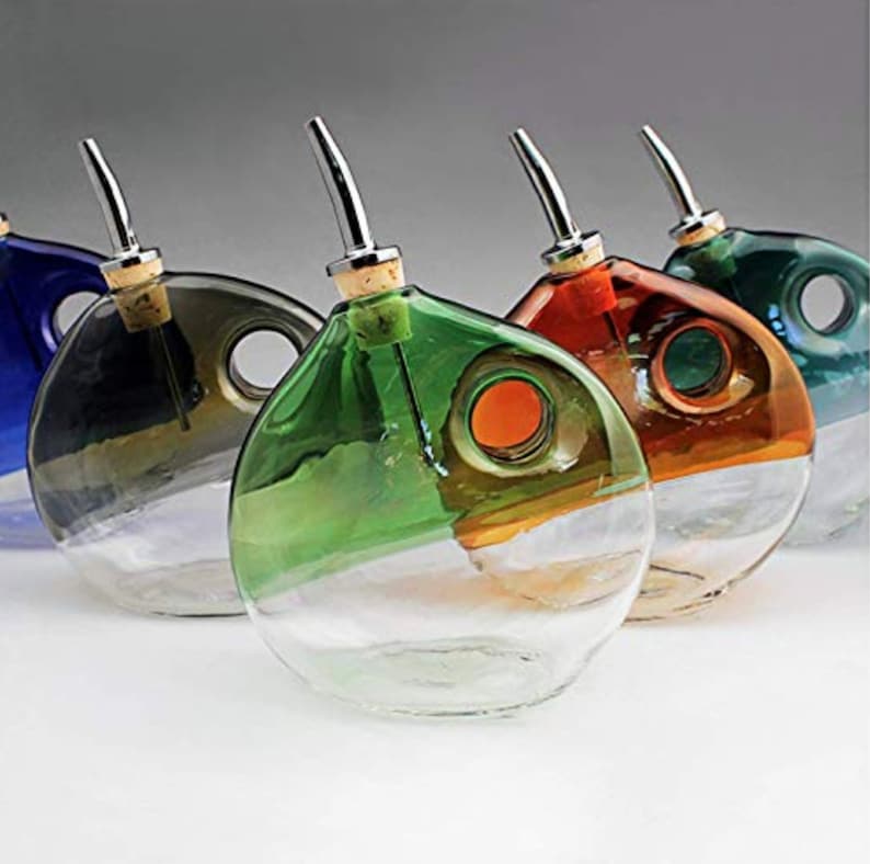 May include: Five glass oil and vinegar bottles with cork stoppers and silver spouts. The bottles are clear with a coloured layer at the bottom. The colours are blue, grey, green, orange, and brown.