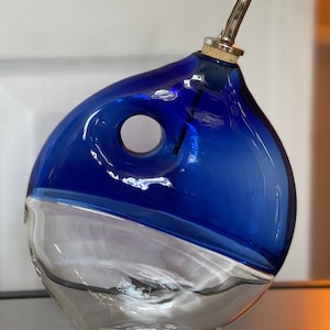 May include: A blue and clear glass oil and vinegar bottle with a spout. The bottle has a unique, rounded shape with a hole in the side.
