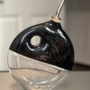 May include: A black and clear glass bottle with a silver spout. The bottle is shaped like a fish and has a hole in the side.