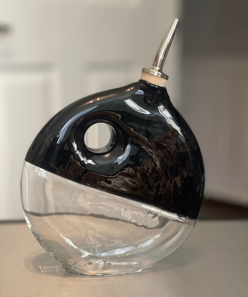 May include: A black and clear glass bottle with a silver spout. The bottle is shaped like a fish and has a hole in the side.