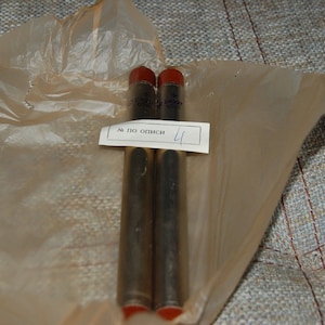 May include: Two silver tubes with red caps, wrapped in brown paper. A white label with the text "№ по описн 4" is attached to the paper.