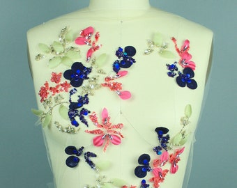 Può includere: Un'applicazione floreale con fiori di tessuto rosa, blu e verde e paillettes. L'applicazione è esposta su un manichino bianco con il testo "COLLAPSIBLE SHOULDER" e il numero "8" sul davanti.