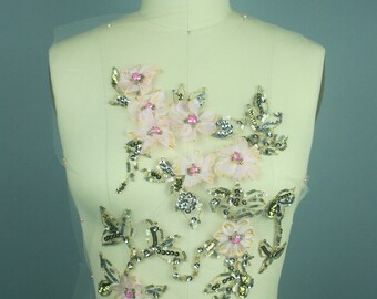 Può includere: Un'applicazione floreale delicata con fiori in tessuto rosa, paillettes dorate e argentate e perline rosa. L'applicazione è esposta su un manichino bianco con il testo "COLLAPSIBLE SHOULDER 8" stampato sul manichino.