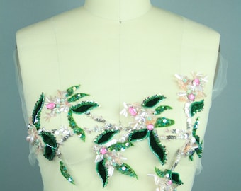 Può includere: Un'applicazione floreale verde e rosa con paillettes e foglie di velluto. L'applicazione è su un manichino bianco.