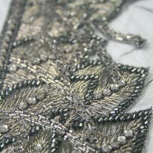 May include: Close-up of a silver and black beaded trim with a leaf design. The trim is made of small beads and sequins.