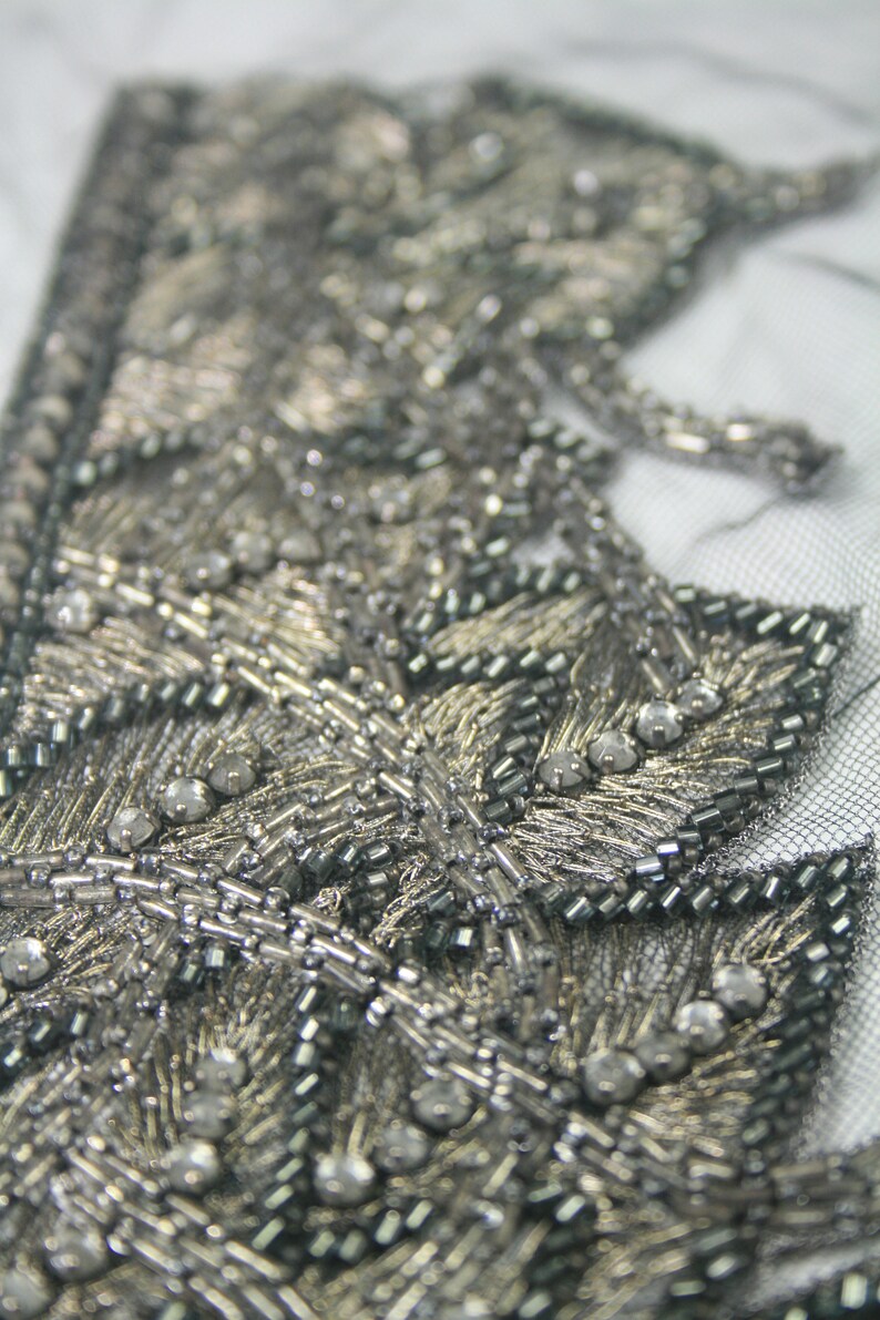 May include: Close-up of a silver and black beaded trim with a leaf design. The trim is made of small beads and sequins.