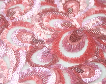 May include: Pink and white sequined fabric with a swirling pattern. The sequins are arranged in a circular pattern, creating a delicate and elegant design.