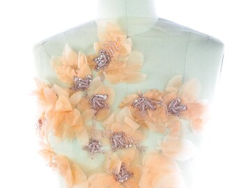 Può includere: Applique di fiori in tessuto color pesca con dettagli perlati. L'applique è su un manichino bianco.