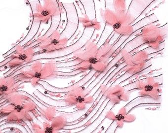 Può includere: Tessuto rosa con decorazioni a perline e applicazioni floreali. Il tessuto è progettato in un motivo ondulato con file di perline e fiori.