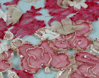 Può includere: Primo piano di un delicato pizzo rosa e beige con ricami floreali e dettagli perlati. Il tessuto ha una texture leggera e trasparente, ideale per creare abiti o accessori.