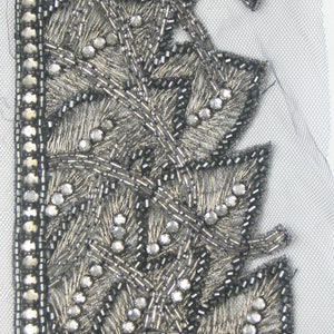May include: Silver beaded trim with a delicate floral design. The trim is on a sheer fabric background.