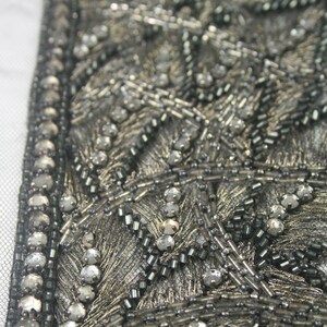 May include: Close-up of a silver and black beaded trim with a geometric pattern. The trim is made of small beads and sequins, and it has a delicate, intricate design.