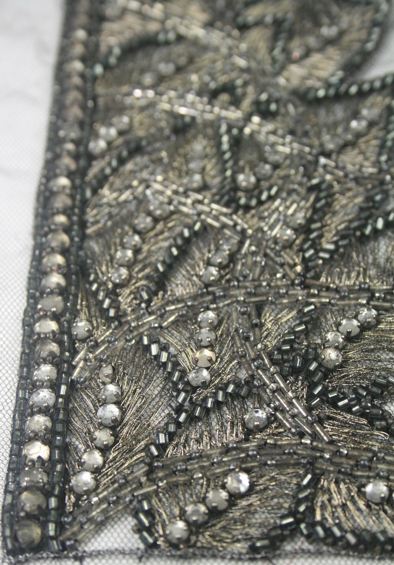 May include: Close-up of a silver and black beaded trim with a geometric pattern. The trim is made of small beads and sequins, and it has a delicate, intricate design.