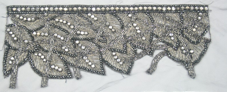 May include: Silver and black beaded trim with a leaf design. The trim has a scalloped edge and is perfect for adding a touch of elegance to any project.