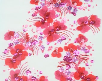 Può includere: Tessuto rosso e rosa con fiori ricamati e paillettes. Il tessuto ha uno sfondo bianco.