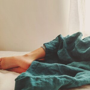 May include: A person is lying on a bed with a teal linen sheet. The sheet is folded over the person's legs and feet.