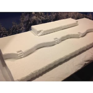 May include: A white foam model of a snowy landscape with three levels and steps leading up to the top level.