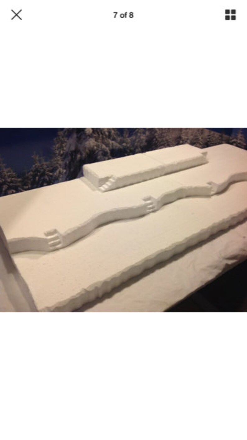 May include: A white foam model of a snowy landscape with three levels and steps leading up to the top level.