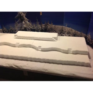 May include: A white, three-tiered, foam display platform with a snowy, wintery theme. The platform has a textured surface and is designed for displaying products or crafts.
