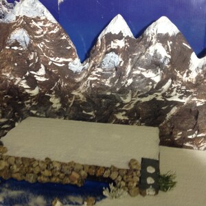 May include: A miniature winter scene with a snowy mountain range backdrop, a small stone wall, and a white snowy surface in the foreground.