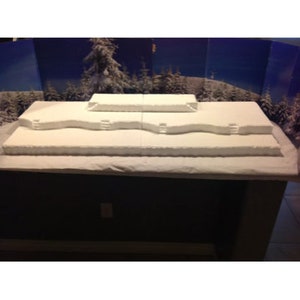 May include: A white, snow-covered, multi-level platform with a blue and white backdrop. The platform is made of styrofoam and has a rough, textured surface.