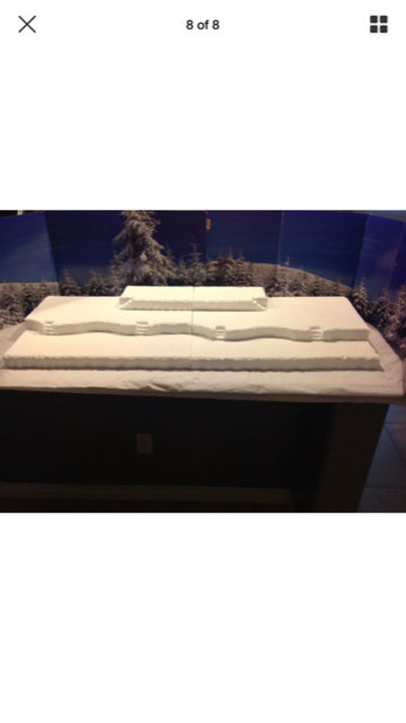 May include: A white, snow-covered, multi-level platform with a blue and white backdrop. The platform is made of styrofoam and has a rough, textured surface.