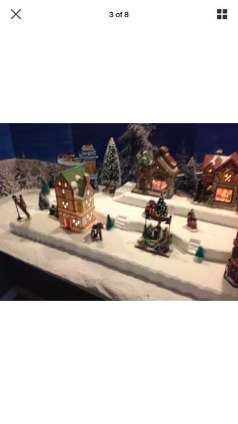 May include: A miniature Christmas village scene with a variety of houses, trees, and figures. The houses are lit up with white lights and there is a small horse and carriage in the foreground.