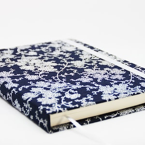 May include: A navy blue journal with a white floral pattern and a white ribbon bookmark.